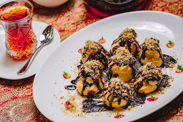 Bovenaanzicht dessert profiteroles met chocolade glazuur en geraspte noten met een glas thee