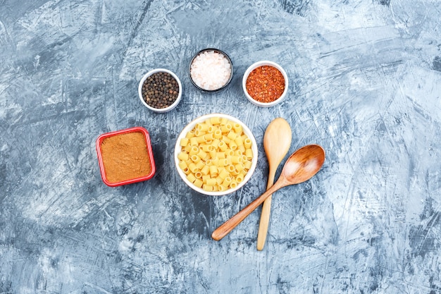 Bovenaanzicht ditalini pasta in witte kom met houten lepels, kruiden op grijze gips achtergrond. horizontaal