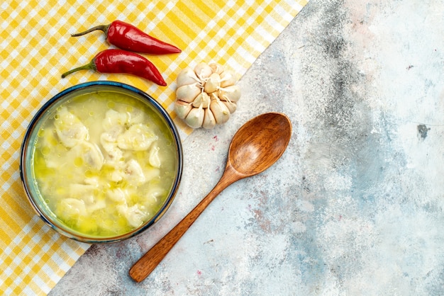 Gratis foto bovenaanzicht dushbara dumplings soep in een kom hete pepers knoflook op gele en witte geruite keuken handdoek houten lepel op naakt oppervlak