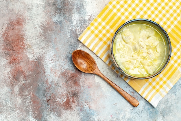 Bovenaanzicht dushbara dumplings soep in een kom op gele en witte geruite keukenhanddoek houten lepel op naakt oppervlak vrije ruimte