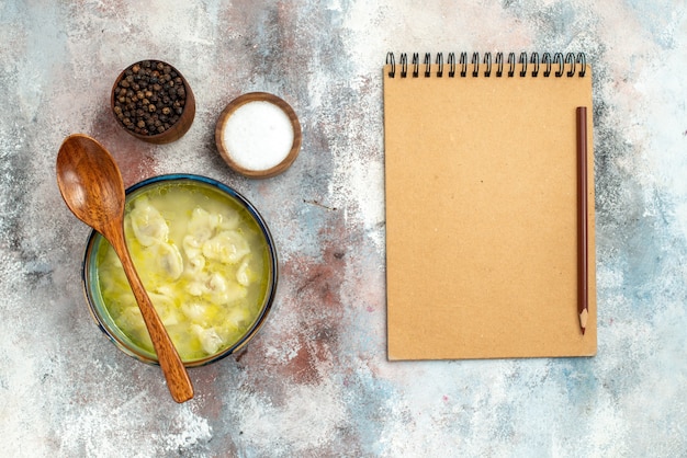 Bovenaanzicht dushbara dumplings soepkommen met zout peper houten lepel op kom een notitieboekje en potlood op naakt oppervlak