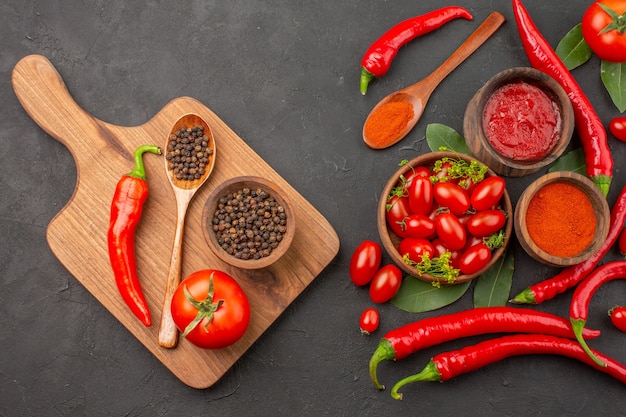 Gratis foto bovenaanzicht een kom cherrytomaatjes rode paprika laurierblaadjes en een kom zwarte peper een lepel een tomaat een rode paprika op de snijplank op zwarte grond