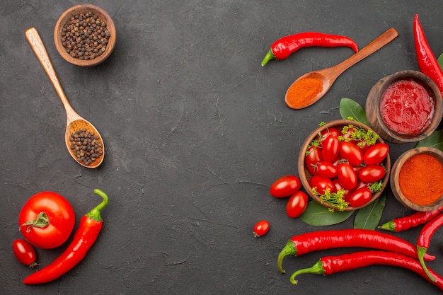 Bovenaanzicht een kom met kerstomaatjes hete rode paprika zwarte peper in een houten lepel kommen ketchup zwarte peper en rode peper poeder op de zwarte tafel