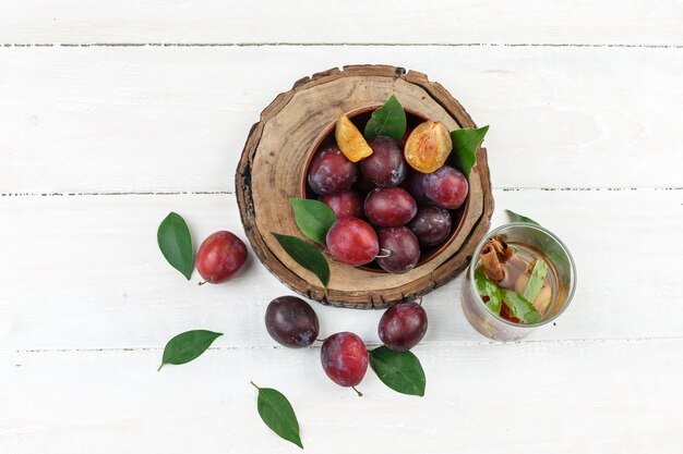 Bovenaanzicht een kom pruimen op een houten bord met detox water en bladeren op witte houten bord tafel. horizontaal