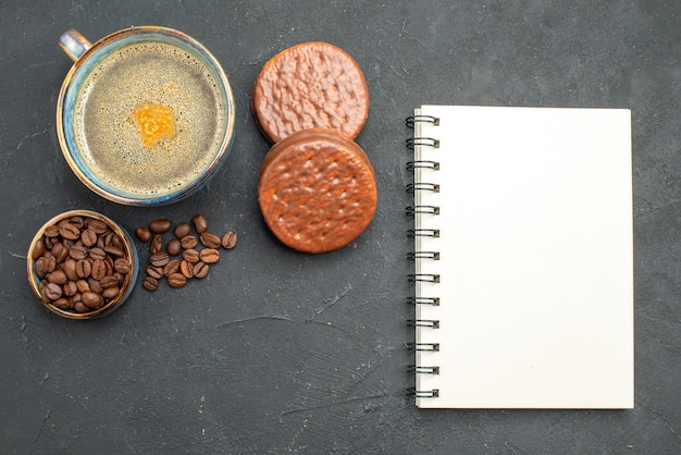 Bovenaanzicht een kopje koffiekom met koffie zaden koekjes een notitieblok op donkere geïsoleerde achtergrond