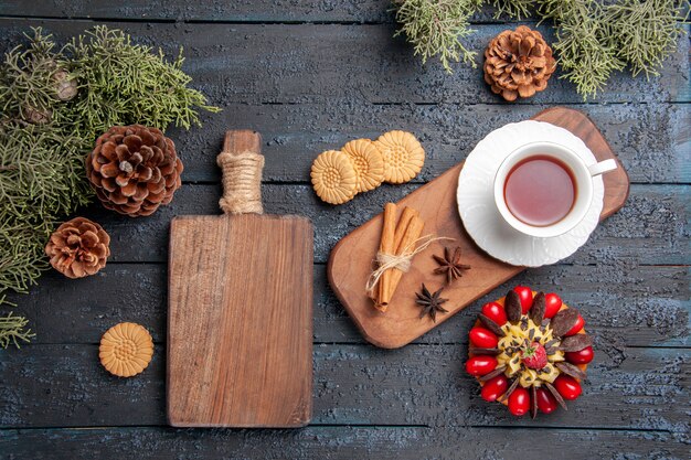 Bovenaanzicht een kopje thee anijs zaden en kaneel op houten serveerschaal koekjes dennenappels bessen cake en snijplank op donkere houten tafel