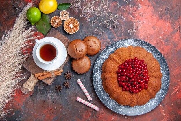 Bovenaanzicht een kopje thee een cake met rode bessen een kopje zwarte thee kaneel op de snijplank