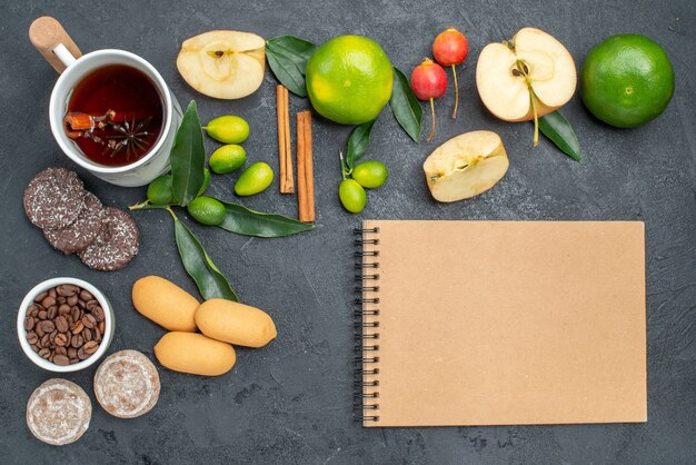 Bovenaanzicht een kopje thee een kopje thee appels bessen citrusvruchten koekjes crème notitieboekje