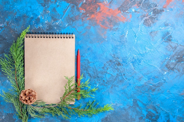 Bovenaanzicht een notebook dennenboom takken dennenappel rood potlood op blauwe achtergrond vrije ruimte