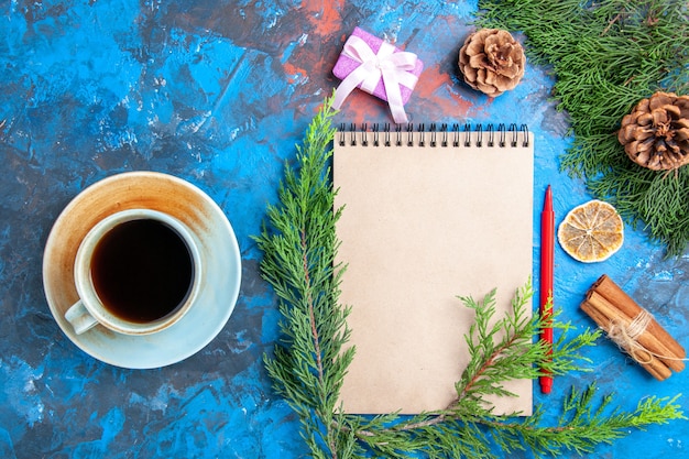 Bovenaanzicht een notebook dennenboom takken rood potlood een kopje thee op blauwe achtergrond