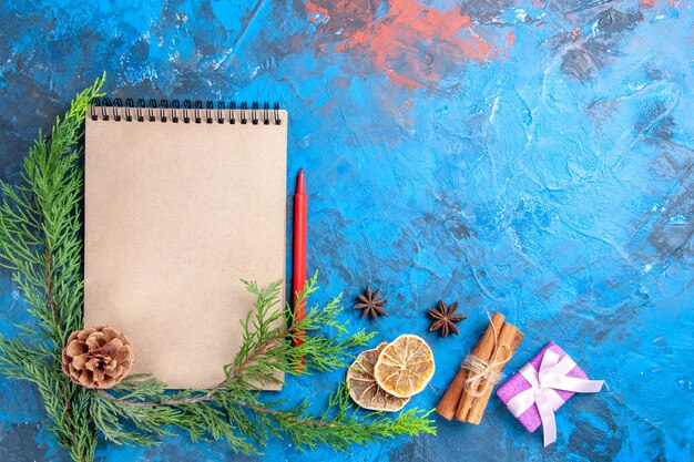 Bovenaanzicht een notitieboekje dennenboom takken dennenappel rood potlood kaneelstokjes anijs gedroogde citroenschijfjes op blauwe achtergrond vrije ruimte