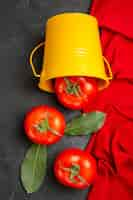 Gratis foto bovenaanzicht emmer met rode tomaten rode handdoek op donkere achtergrond