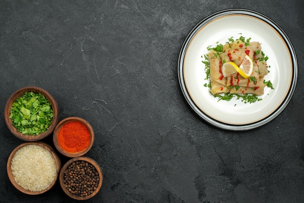 Bovenaanzicht eten op witte plaat witte plaat van gevulde kool met sauskruiden en citroen aan de rechterkant en kommen met specerijen, rijstkruiden en saus aan de linkerkant van zwarte tafel