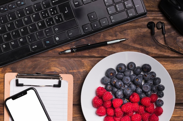 Bovenaanzicht fruit op plaat en toetsenbord met lege notebook en telefoon