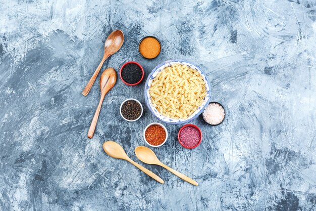 Bovenaanzicht fusilli pasta in kom met kruiden, houten lepels op grijze gips achtergrond. horizontaal