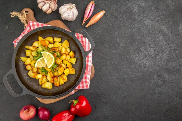 Bovenaanzicht gebakken aardappelen in pan met groenten op de donkere achtergrond