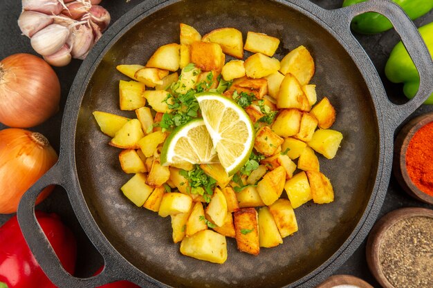 Bovenaanzicht gebakken aardappelen in pan met verschillende kruiden en groenten op de donkere achtergrond