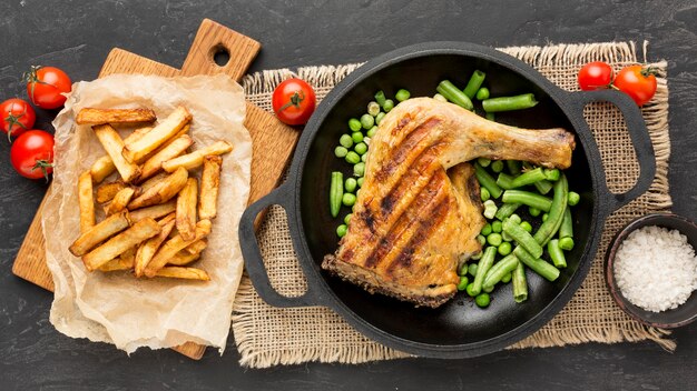 Bovenaanzicht gebakken kip en peulen in pan met aardappelen en tomaten