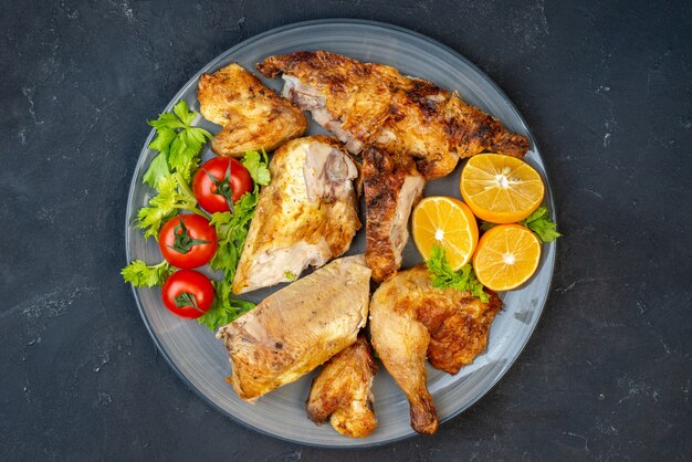 Bovenaanzicht gebakken kip verse tomaten schijfjes citroen op ronde plaat op zwarte tafel