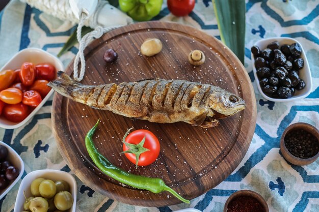 Bovenaanzicht gebakken vis met tomaat chili peper champignons op een dienblad met olijven en kruiden op tafel