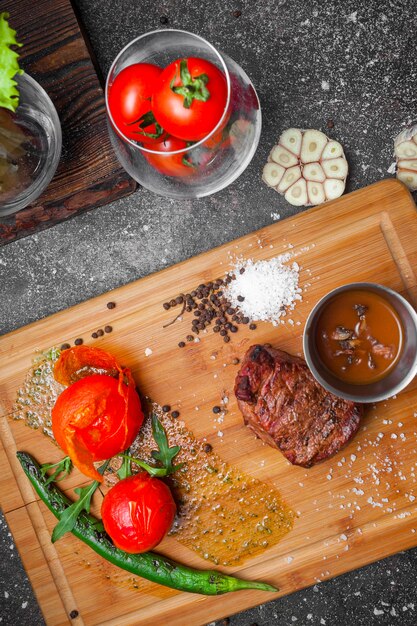 Bovenaanzicht gegrild vlees met tomaat en papier en saus in steak board