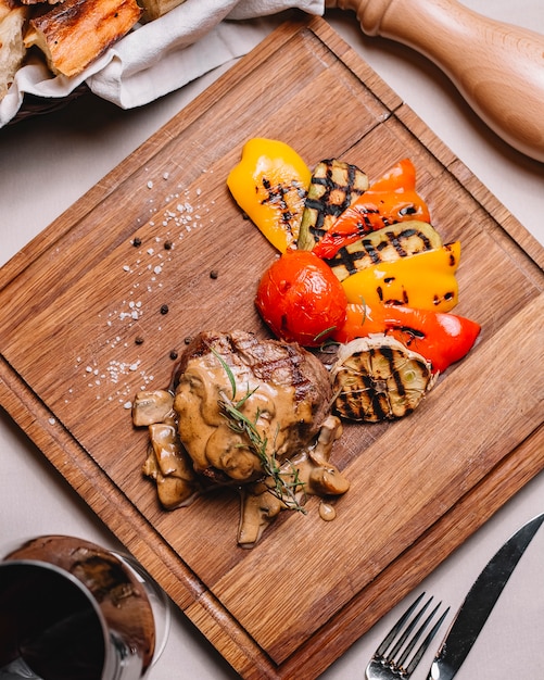 Bovenaanzicht gegrilde steak met courgette paprika tomaat champignons saus zout en zwarte peper op een bord