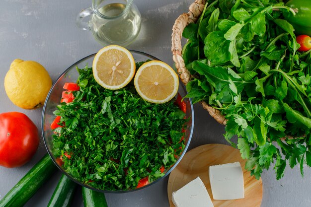 Bovenaanzicht gehakte greens in glazen kom met tomaten, kaas, citroen op grijze ondergrond