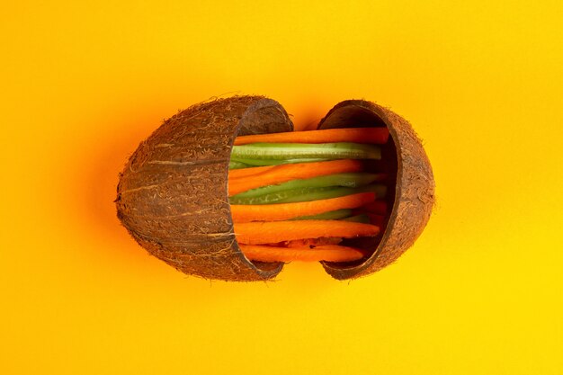 Bovenaanzicht gehakte wortelen met komkommer in een kokosnoot op geel