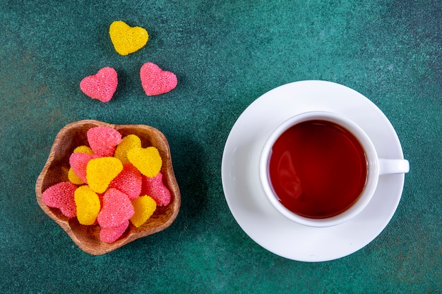 Bovenaanzicht gekleurde marmelade in de vorm van een hart met een kopje thee op groen