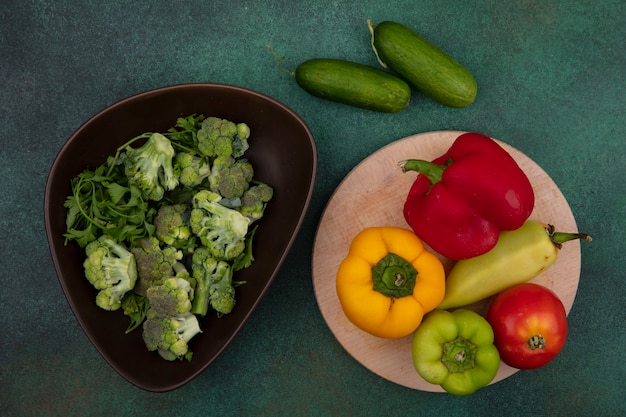 Bovenaanzicht gekleurde paprika met tomaat op een stand en komkommers met broccoli op een groene achtergrond
