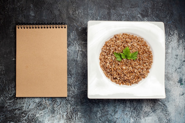 Bovenaanzicht gekookt boekweit in plaat met notitieblok op grijze achtergrond koken maaltijdboon foto eten