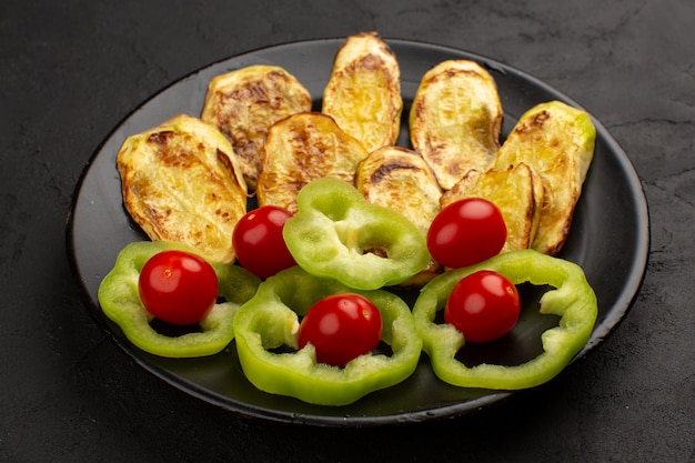 bovenaanzicht gekookte aubergine samen met gesneden groene paprika en hele tomaten in zwarte plaat op het donker