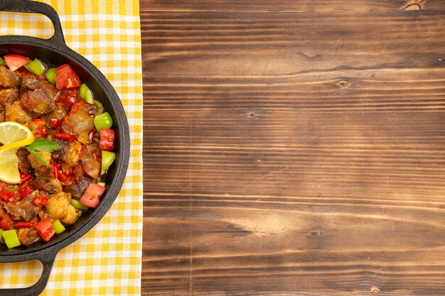 Bovenaanzicht gekookte groentemaaltijd met vlees en gesneden paprika in pan op het bruine houten bureau