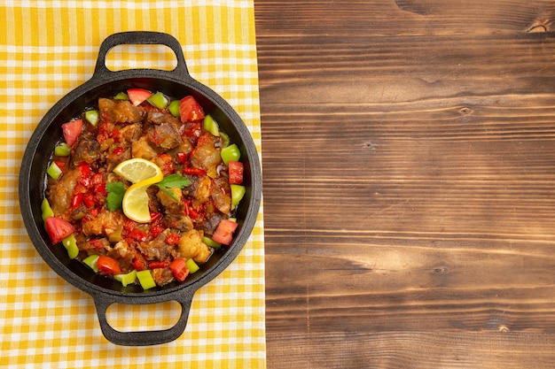 Bovenaanzicht gekookte groentemaaltijd met vlees en gesneden paprika in pan op het bruine houten bureau