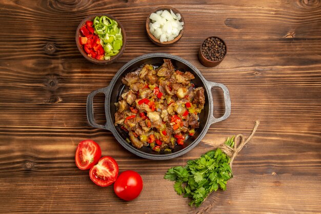 Bovenaanzicht gekookte groentemaaltijd met vlees en vers gesneden paprika op houten bruin bureau