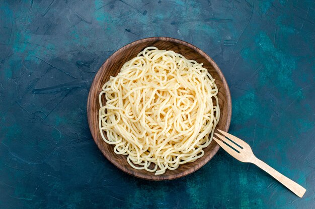 Bovenaanzicht gekookte Italiaanse pasta binnen ronde houten plaat op blauwe achtergrond pasta Italië eten diner deeg