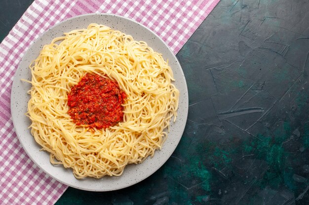 Bovenaanzicht gekookte Italiaanse pasta met gehakt tomatenvlees op het donkerblauwe oppervlak