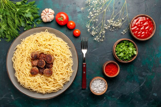 Bovenaanzicht gekookte Italiaanse pasta met gehaktballen, kruiden en Groenen op het donkerblauwe oppervlak