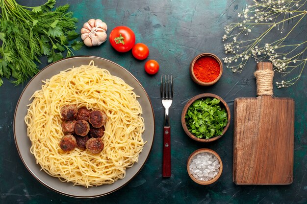 Bovenaanzicht gekookte Italiaanse pasta met gehaktballetjes, kruiden en groenten op het donkerblauwe bureau