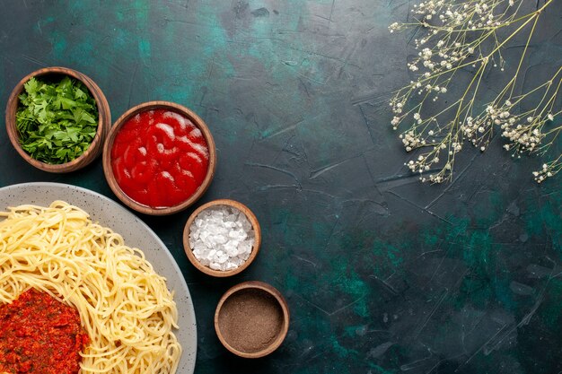 Bovenaanzicht gekookte Italiaanse pasta met vlees en verschillende kruiden op het donkerblauwe oppervlak