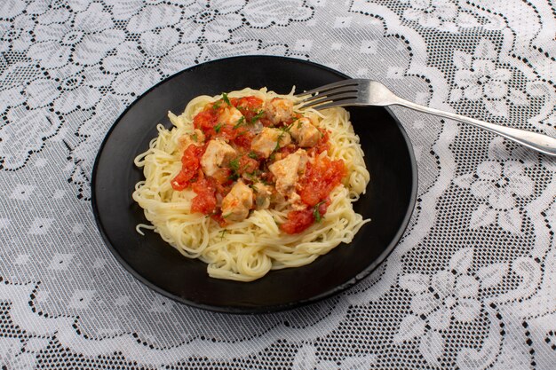 bovenaanzicht gekookte pasta lekker met plakjes kip en tomatensaus in zwarte plaat op tafel