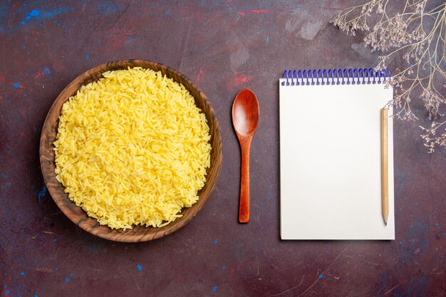 Bovenaanzicht gekookte rijst heerlijke maaltijd in bruine plaat op donker bureau