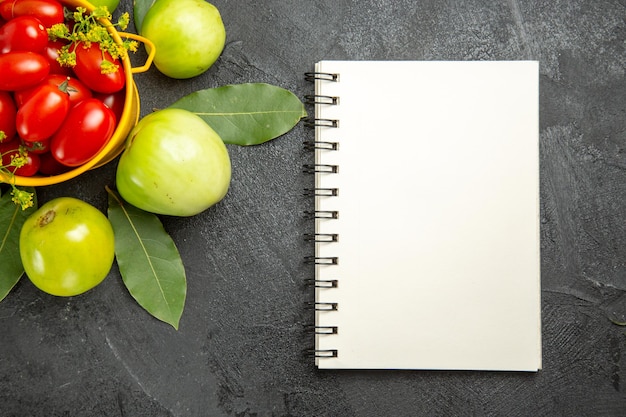 Bovenaanzicht gele emmer gevuld met kerstomaatjes en dille bloemen groene tomaten laurierblaadjes en een notitieboekje op donkere ondergrond