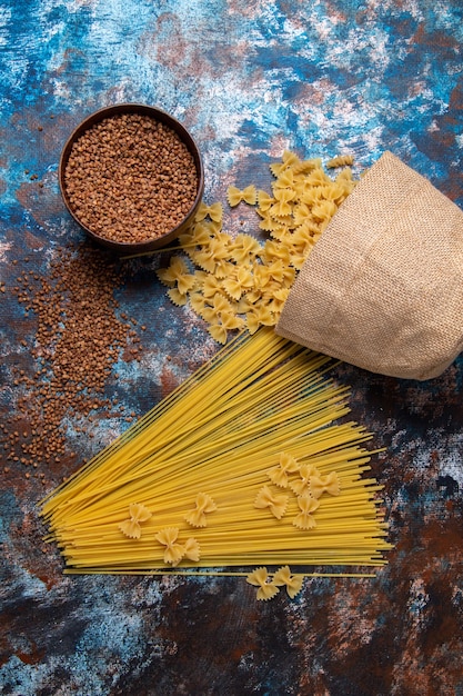 Bovenaanzicht gele rauwe pasta lang gevormd en weinig met boekweit helemaal over de gekleurde achtergrond pasta italië voedselmaaltijd