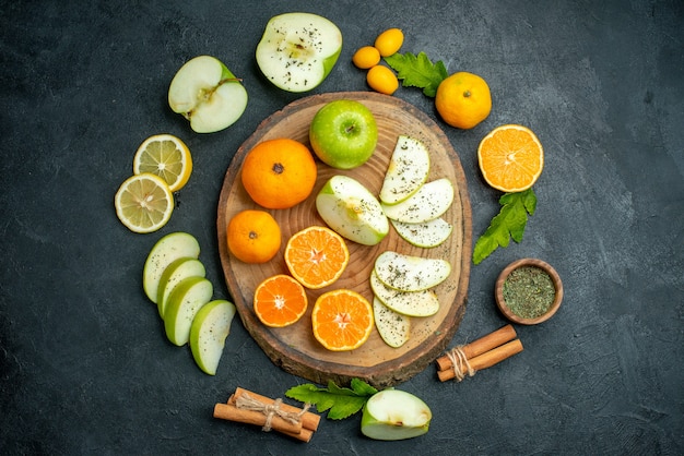 Bovenaanzicht gesneden appels en mandarijnen op rustieke ronde bord kaneel vastgebonden met touw cumcuat en andere spullen rond bord op donkere tafel