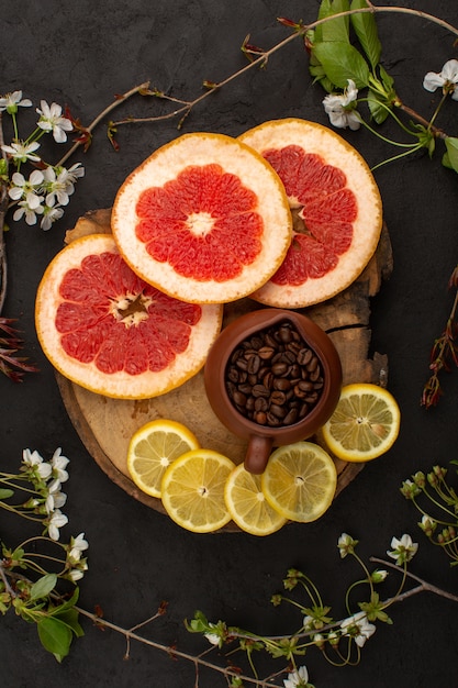 Gratis foto bovenaanzicht gesneden fruit citrusvruchten zoals grapefruit en citroen samen met koffie op de bruin houten bureau en donkere vloer