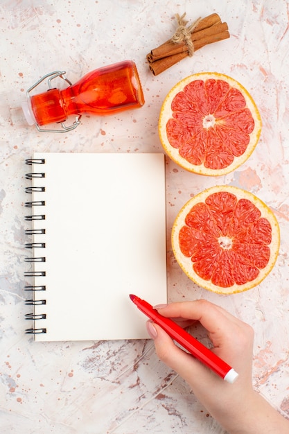 Bovenaanzicht gesneden grapefruits kaneelstokjes fles kladblok rode marker in vrouwelijke hand op naakt oppervlak