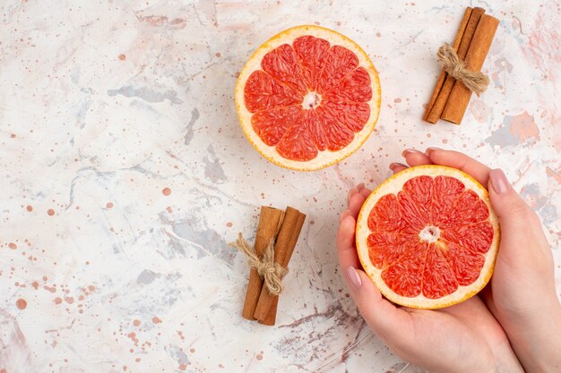 Bovenaanzicht gesneden grapefruits kaneelstokjes gesneden grapefruit in vrouwelijke hand op naakt oppervlak vrije ruimte