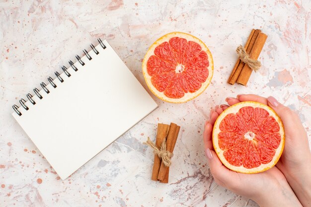 Bovenaanzicht gesneden grapefruits kaneelstokjes notebook gesneden grapefruit in vrouwelijke hand op naakt oppervlak