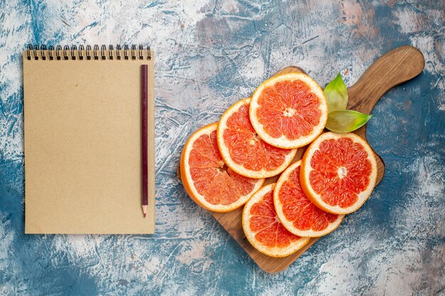 Bovenaanzicht gesneden grapefruits op snijplank notebook en potlood op blauw wit oppervlak